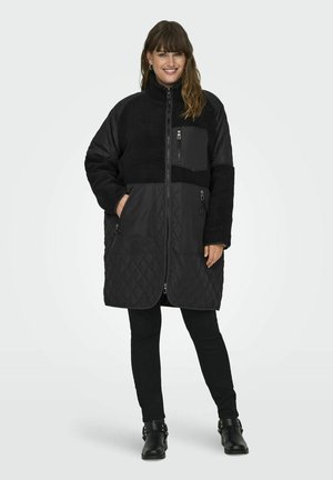 Black hybrid coat featuring a fuzzy upper and quilted lower section, front zip, side pockets, and a high collar for added warmth.