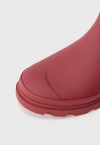 Punane kummist saabas ümmarguse varbaga, sileda tekstuuriga ja paksu tallaga, millel on horisontaalsed mustrid, et tagada haarduvus.
