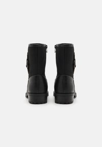 Par de botas negras hasta medio pantorrilla con cremalleras a los lados, suelas robustas y hebillas decorativas, mostradas desde atrás sobre un fondo liso.