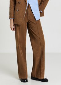 Braune Cordhose mit weitem Bein und vertikalen Streifen, kombiniert mit einem hellblauen Hemd und schwarzen Lederschuhen. Strukturierter Stoff und maßgeschneiderte Passform.