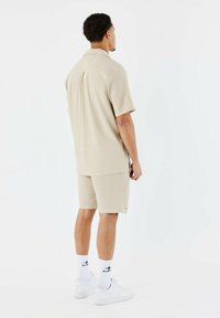 Polo de color beige con textura y pantalones cortos a juego, ambos de corte relajado. Zapatillas blancas y calcetines con patrón completan el conjunto.