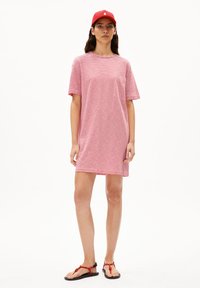 Rood-wit gestreepte jurk met korte mouwen en een borstzakje, gecombineerd met zwarte sandalen met rode accenten en een rode pet.