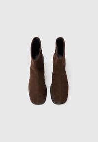 Bottines en daim marron au design épuré, forme effilée et fermetures éclair sur le côté. Surface texturée avec une semelle noire lisse.