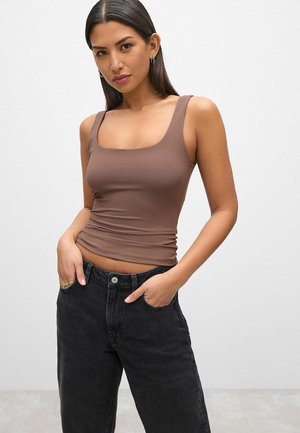 Top en tank marron ajusté avec un décolleté carré, texture lisse et larges bretelles, associé à un jean en denim noir taille haute.
