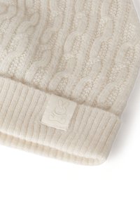 Kremowa dzianinowa czapka z wzorem warkocza i ściągaczem. Na ściągaczu przyszyta jest mała metka z logo zająca.