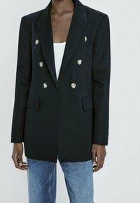 Svart dubbelknäppt kavaj med silverfärgade knappar, pekade slag och två framfickor med klaff, tillsammans med blå jeans.