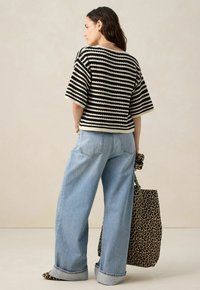 Haut en tricot rayé noir et crème, associé à un jean taille haute bleu clair et un sac fourre-tout à imprimé léopard. Coupe décontractée et manches courtes.