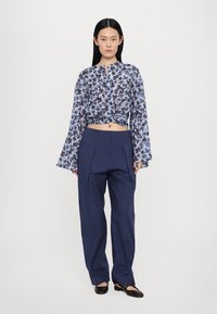 Blue floral patterned long-sleeve blouse with a knotted front, paired with navy high-waisted wide-leg trousers and black slip-on shoes.