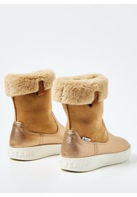 Brune kunstmocka-støvler med en fluffy beige manchet, der har en skinnende rosaguldsaccent på hælen og en hvid tekstureret sål.