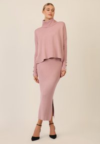 Helles rosa gestricktes Rollkragensweatshirt mit lockerer Passform und geripptem Textur, kombiniert mit einem passenden gerippten Rock mit seitlichem Schlitz und geknöpften Manschetten.