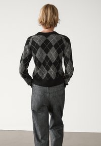 Pull noir et gris à motif argyle avec une texture en tricot, associé à un pantalon rayé gris. Le design présente une silhouette ajustée.