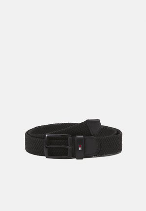 Ceinture en tissu tissé noir avec boucle en métal noir et petite étiquette rectangulaire portant un logo près de l'extrémité de la boucle, présentée enroulée sur fond blanc.