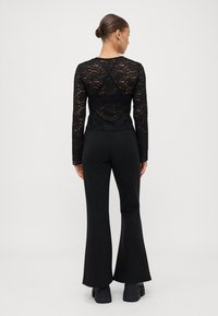 Schwarzes Spitzenoberteil mit langen Ärmeln und Rundhalsausschnitt, kombiniert mit schwarzen, ausgestellten Hosen. Die Spitze weist ein florales Muster und eine transparente Textur auf.