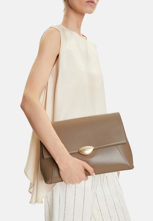 Žena ve světle béžovém topu bez rukávů a bílých pruhovaných kalhotách, držící velkou obdélníkovou taupe kabelku se zlatým zapínáním.