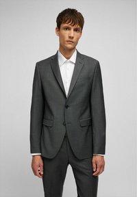 Grau Anzug mit strukturierter Oberfläche, ein einzelner Frontknopf, schmale Revers und zwei Vorderjackentaschen. Weißes Hemd mit Kragen darunter.
