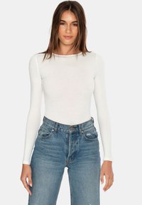 Witte langemouwtop gemaakt van zacht materiaal, gecombineerd met hoog-gewaste vervaagde blauwe jeans met zichtbare stiksels en een klassieke vijf-pocket ontwerpen.