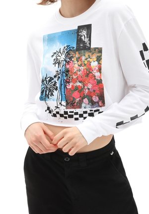 Crop top blanc à manches longues avec un imprimé coloré de palmiers, de fleurs et une statue en noir et blanc, associé à un pantalon noir.