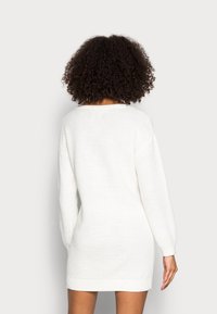 Vit stickad tröjdress med lång ärm, ribbat fåll och texturerat tyg. Har en rund halsringning och en avslappnad passform.