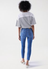 Pruhované bílé a černé tričko s uzlem na zádech, spárované s přiléhavými modrými džíny s kapsami na zadní straně a minimáln�ím opotřebením.