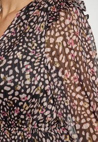 Schwarzes und pinkes gemustertes Kleid mit Rüschenshirts aus durchsichtigem Stoff, das ein gepunktetes Design und goldene Akzente auf einem leichten Material zeigt.