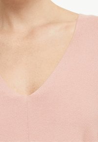 Jasnoróżowy sweter z dzianiny z dekoltem w kształcie litery V, posiadający teksturowane wykończenie, podkreślający gładki, miękki materiał oraz minimalne detale szycia.