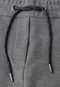 Grå texturerade joggers med dragsko, med en svart snodd och metalltips. Fickor syns på framsidan.