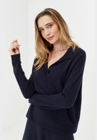 Pull noir marine avec un col, des poignets et un ourlet côtelés. Texture douce avec une coupe décontractée. Petit détail d'accent rouge sur le côté.