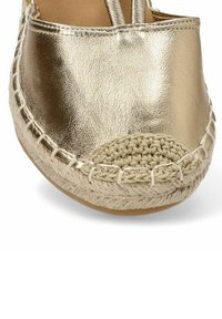Zapato de espadrille metálico dorado con una punta de yute trenzado y borde cosido. Presenta una superficie suave y forma redondeada.