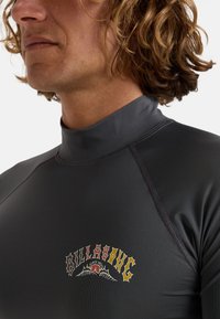 Kortsleeve grå rash guard tillverkad av glatt, elastiskt material. Har en färgglad logotyp med en berg- och hjärtdesign på bröstet.