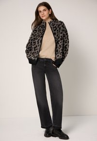 Kurtka w panterkę, miękka, z wysokim kołnierzem, zestawiona z beżowym, prążkowanym swetrem i czarnymi jeansami o prostych nogawkach. Do kompletu czarne botki za kostkę.