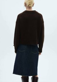 Brauner Strickpullover mit lässiger Passform und geripptem Saum, kombiniert mit einem dunklen Jeansrock und knielangen glänzenden braunen Stiefeln.