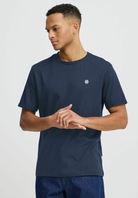 Tamsiai mėlynas medvilninis trumpomis rankovėmis marškinėliai su apvali kaklo iškirpte ir mažu baltu logotipu ant krūtinės. Minkšta tekstūra ir atsitiktinis dizainas.