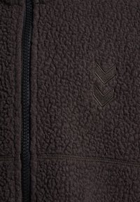 Czarny teksturowany materiał z polaru z czarnym plastikowym zamkiem błyskawicznym i dwoma wyhaftowanymi szewronami po prawej stronie.