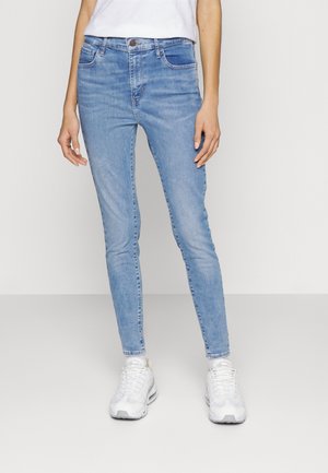 Jeans de denim azul ajustados con diseño de cinco bolsillos, un lavado descolorido y detalles de costura sutiles, combinados con zapatillas deportivas blancas.