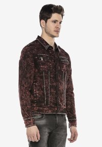 Rote und schwarze, ausgebleichte Jeansjacke mit Metallnieten, zwei Reißverschluss-Brusttaschen und Knopfverschluss. Verfügt über einen klassischen Kragen und lange Ärmel.