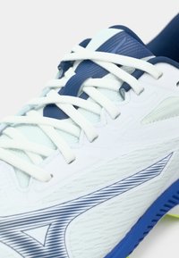 Scarpa da corsa bianca con tomaia in mesh testurizzato, dettagli blu e lacci bianchi. Presenta un motivo a zigzag sul lato e una suola ammortizzata.