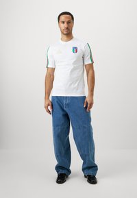 Λευκό βαμβακερό T-shirt με τα χρώματα της ιταλικής σημαίας στους βραχίονες, διαθέτει λογότυπο και χρυσές λεπτομέρειες. Συνδυάζεται με φαρδιά μπλε τζιν παντελόνια.