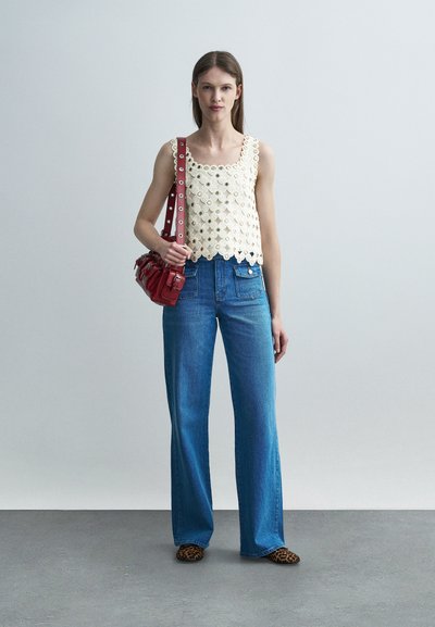 Femme portant un haut en crochet blanc sans manches, un jean taille haute bleu, des chaussures imprimé léopard et un sac à bandoulière en cuir rouge.