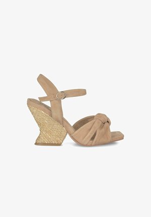 Sandales compensées en suède beige avec un design de orteil noué, une sangle de cheville réglable et un accent en texture tissée sur le talon.