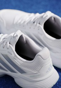 Ζευγάρι λευκά αθλητικά παπούτσια με ανοιχτογκρι ρίγες σε μπλε επιφάνεια, εστιάζοντας στις λεπτομέρειες της φτέρνας και των κορδονιών.