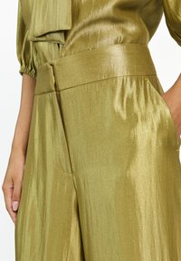 Metallisch olijfgroene broek met een brede tailleband en zijzakken. Gladde textuur met een subtiele glans, met plooidetails.