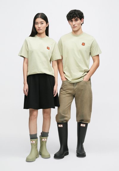 Svetlozelené tričká s malým oranžovým logom, čierna sukňa, khaki nohavice, šedé ponožky a gumové topánky v zelenej a čiernej farbe s detailom loga.