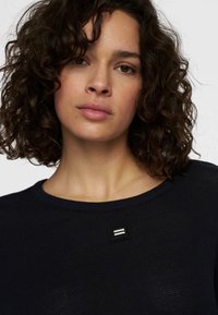 Maglione nero lavorato a maglia con scollatura rotonda, caratterizzato da un motivo testurizzato e un piccolo logo ricamato sul davanti.