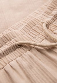 Gros plan d'une ceinture élastique beige en tissu avec un cordon sur un pantalon ou un short à texture douce.