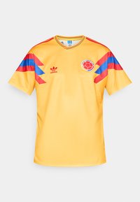 Maglietta da calcio gialla con accenti blu e rossi sulle maniche. Presenta scollo rotondo, logo Adidas e logo circolare della squadra sul petto.