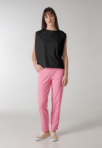 Top nero senza maniche realizzato in morbido tessuto, abbinato a pantaloni aderenti rosa chiaro. I pantaloni presentano tasche anteriori e un design casual.
