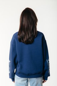 Felpa oversize blu navy con maniche lunghe e polsini a costine. Presenta testo grafico bianco e motivi sulla manica sinistra e sul retro.