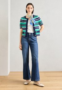 Cardigan à boutons avec des rayures horizontales vertes et marine, associé à un jean bleu taille haute évasé et des ballerines beige clair. Écharpe nouée autour du cou.
