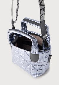 Μικρή μεταλλική ασημί καπιτονέ τσάντα με διπλές λαβές, μαύρο φερμουάρ και ρυθμιζόμενο γκρι υφασμάτινο λουράκι ώμου με μαύρο κείμενο.