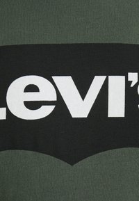 T-paita, jossa on vihreä ja musta värimaailma. Suuri valkoinen "Levi's" -logo on näkyvästi esillä edessä rohkealla fontilla.